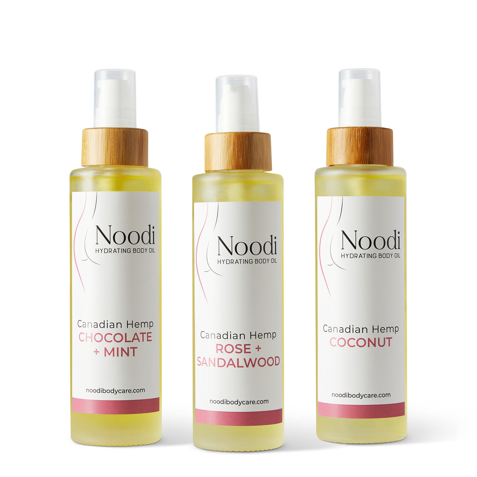 Three bottles of Noodi Hydrating Body Oil in flavors: Chocolate + Mint, Rose + Sandalwood, and Coconut, with wooden caps.